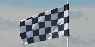 Symbolic image of a black and white patterned target flag waving in the wind. A cloudy sky can be seen in the background.