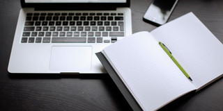 Laptop, smartphone and notebook with pen lying on a table.