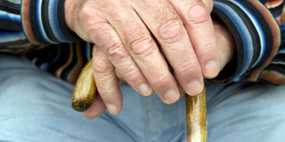 Old person hands are holding a cane.