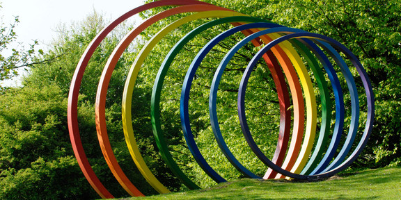 Große bunte Spektralringe aus Stahl stehen auf grünem Rasen.