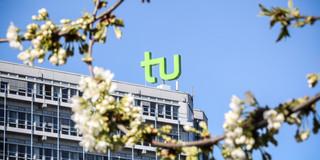 Kirschblüten und das Mathegebäude mit dem TU-Logo im Hintergrund.
